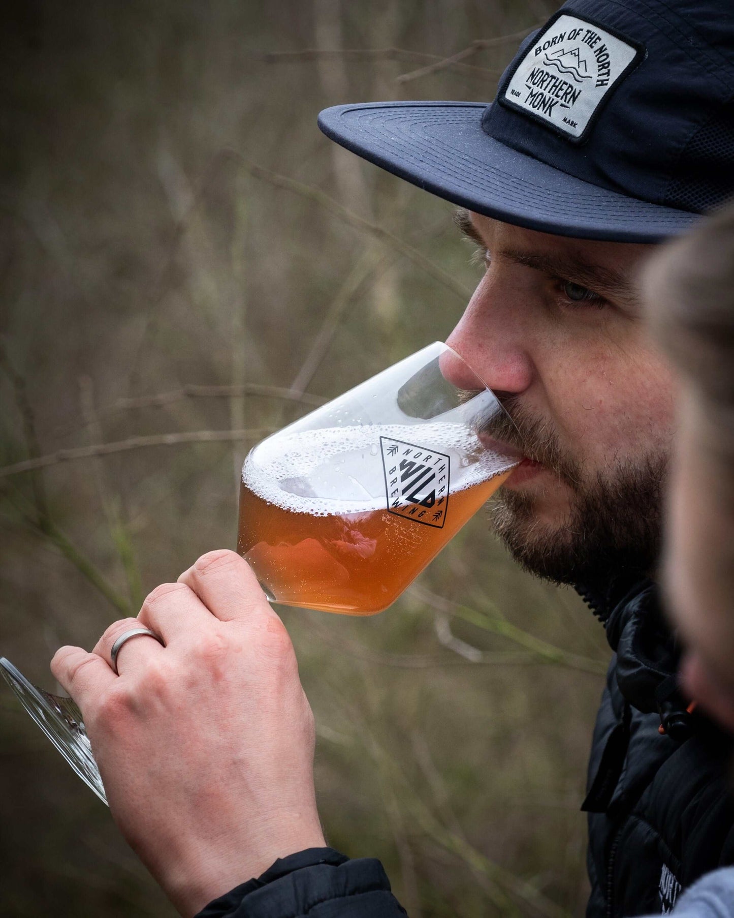 Man enjoying a glass of Northern Wild 006 beer cider hybrid outdoors, highlighting its unique color and craftsmanship.