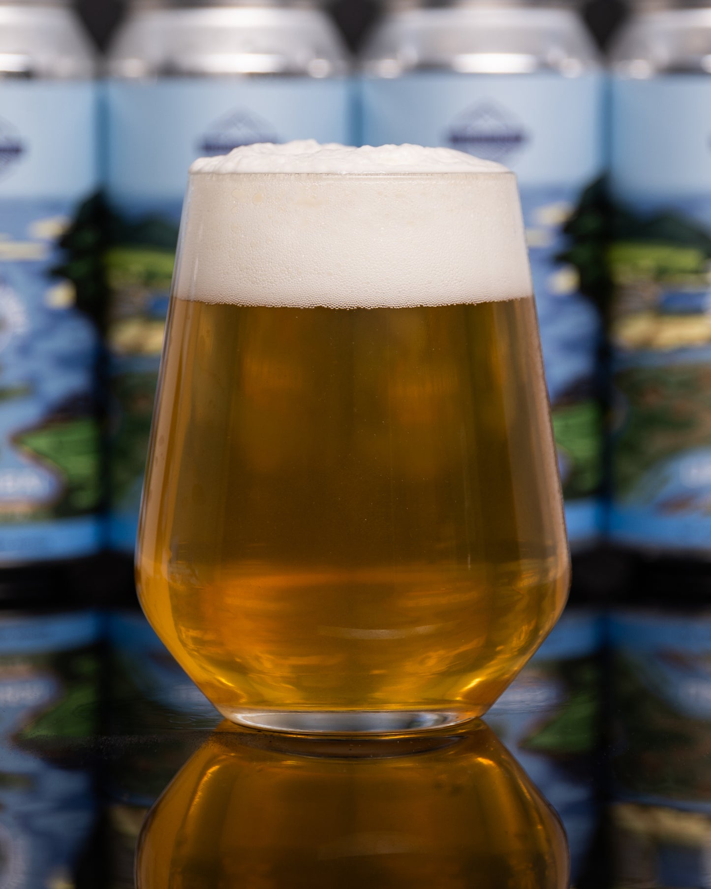 Glass of clean bright IPA with a blurred background of beer cans