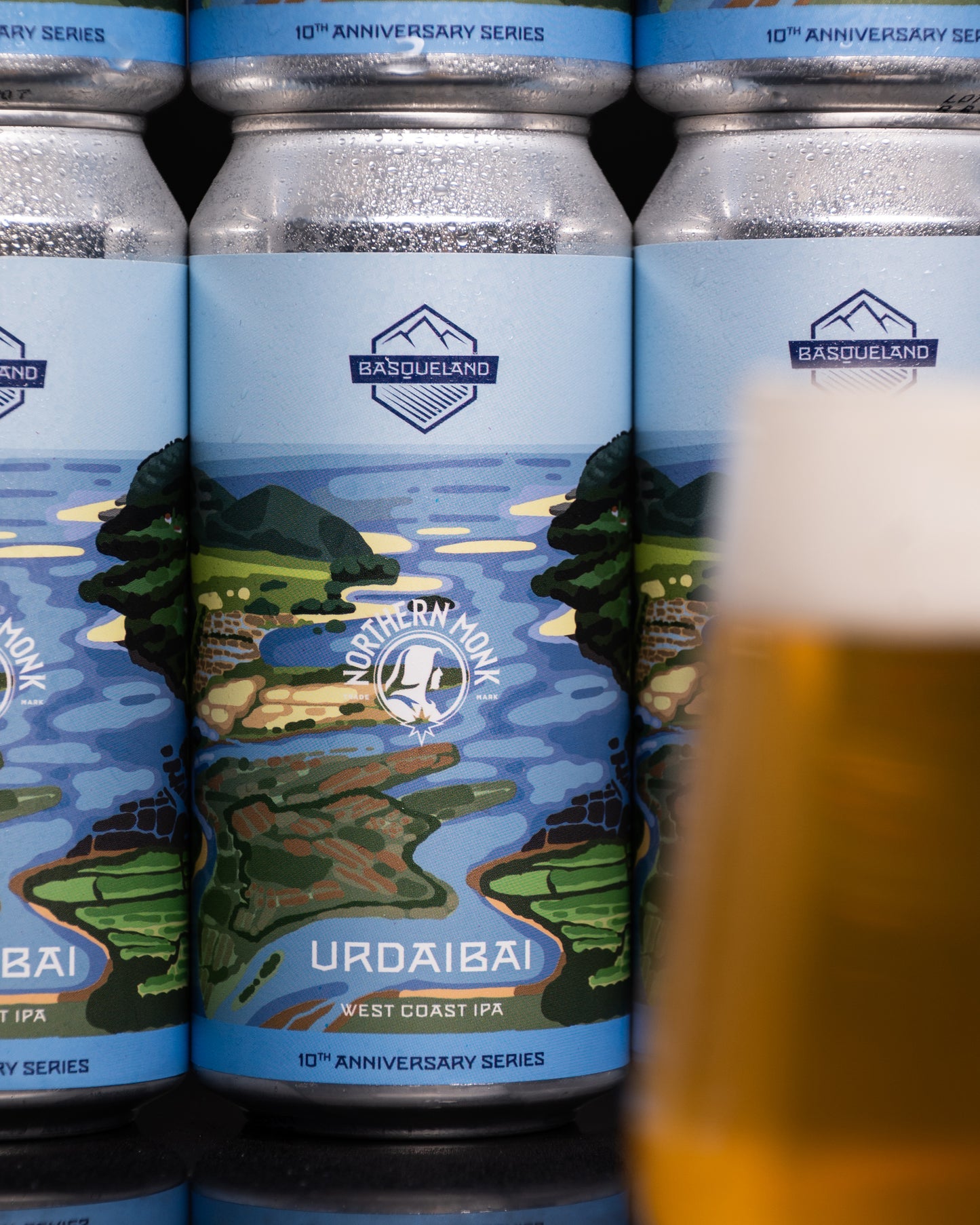 Beer cans with 'Northern Monk' and Basqueland branding and a glass of beer in the foreground.