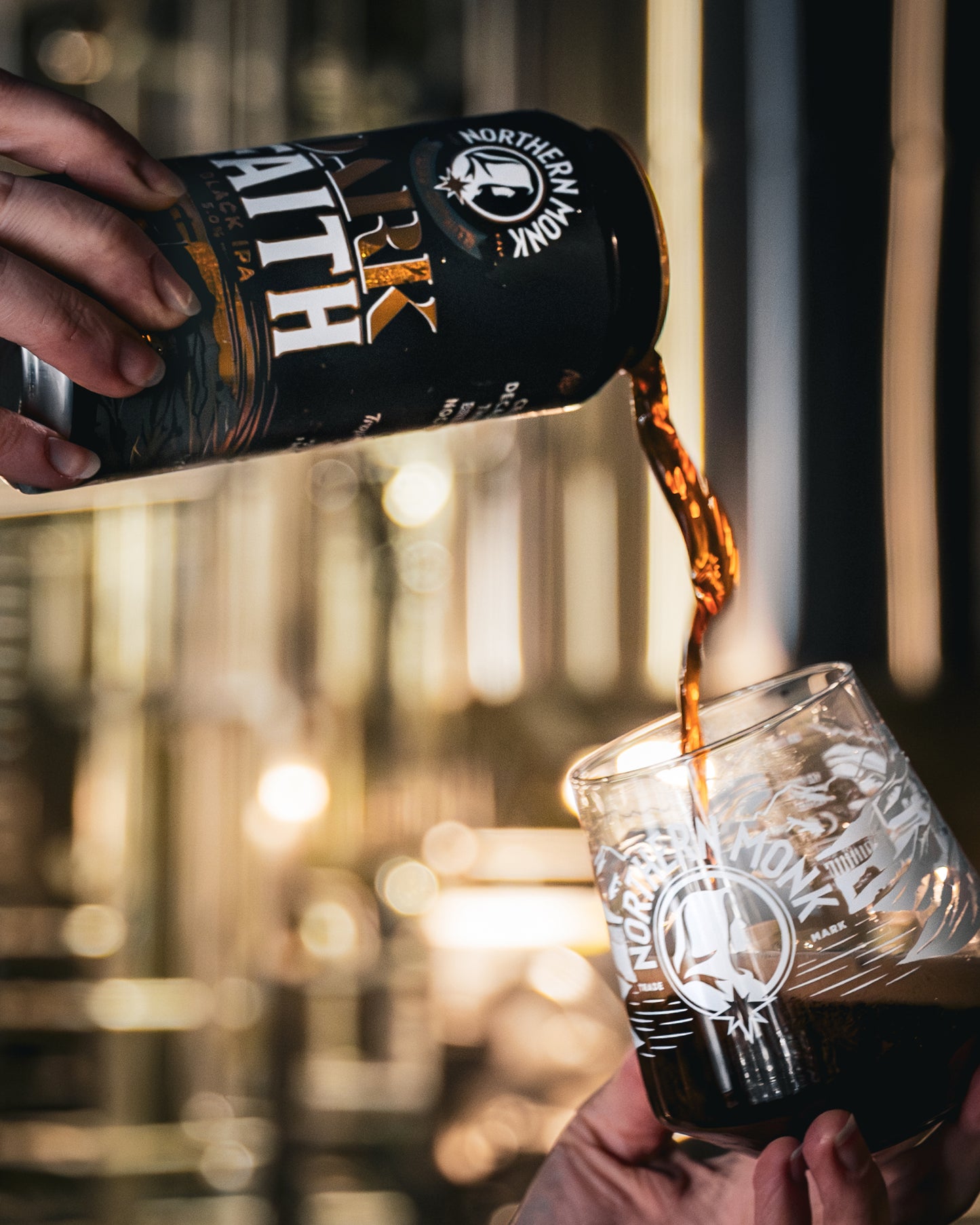 Person pouring dark beer from a can labeled 'Northern Monk into a glass with a blurred background.