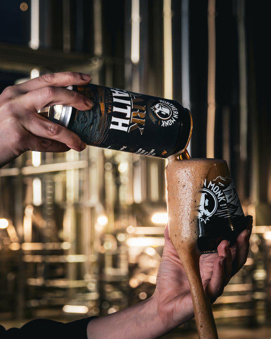 Person pouring a Dark Faith beer into a glass as brown foam overflows