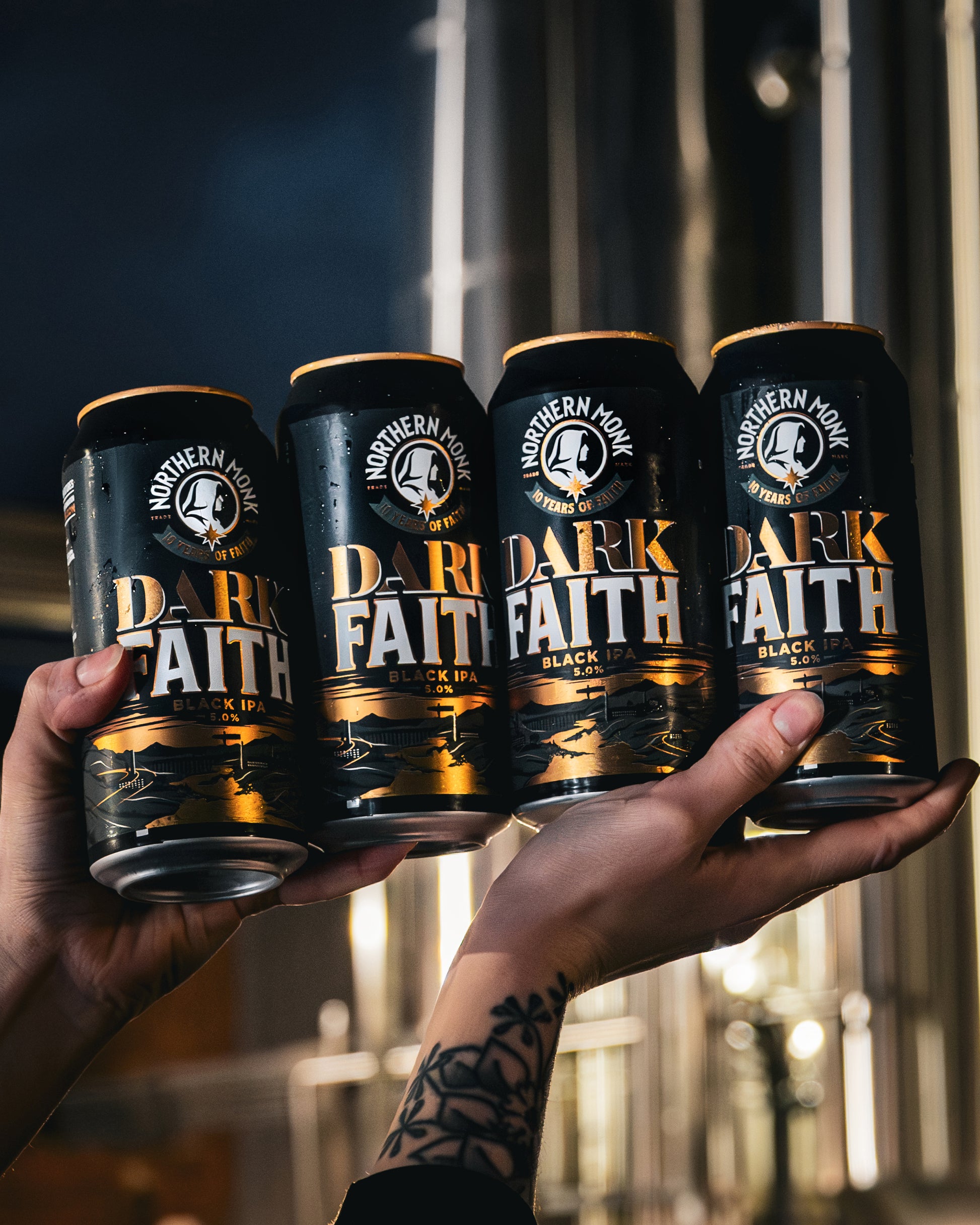 Four cans of 'Dark Faith' beer held up against a blurred background.