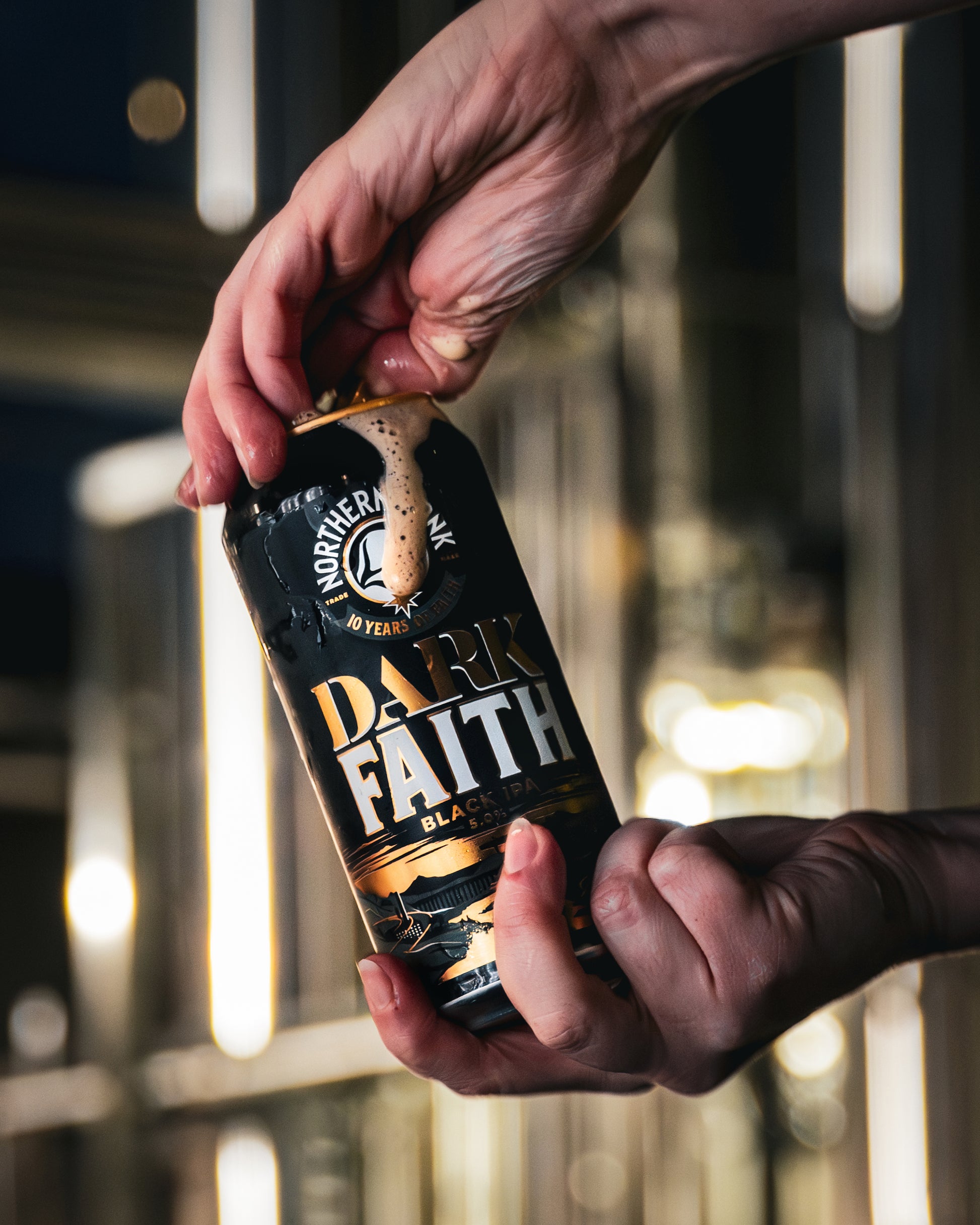Hand opening a can of 'Dark Faith' beer with a blurred background