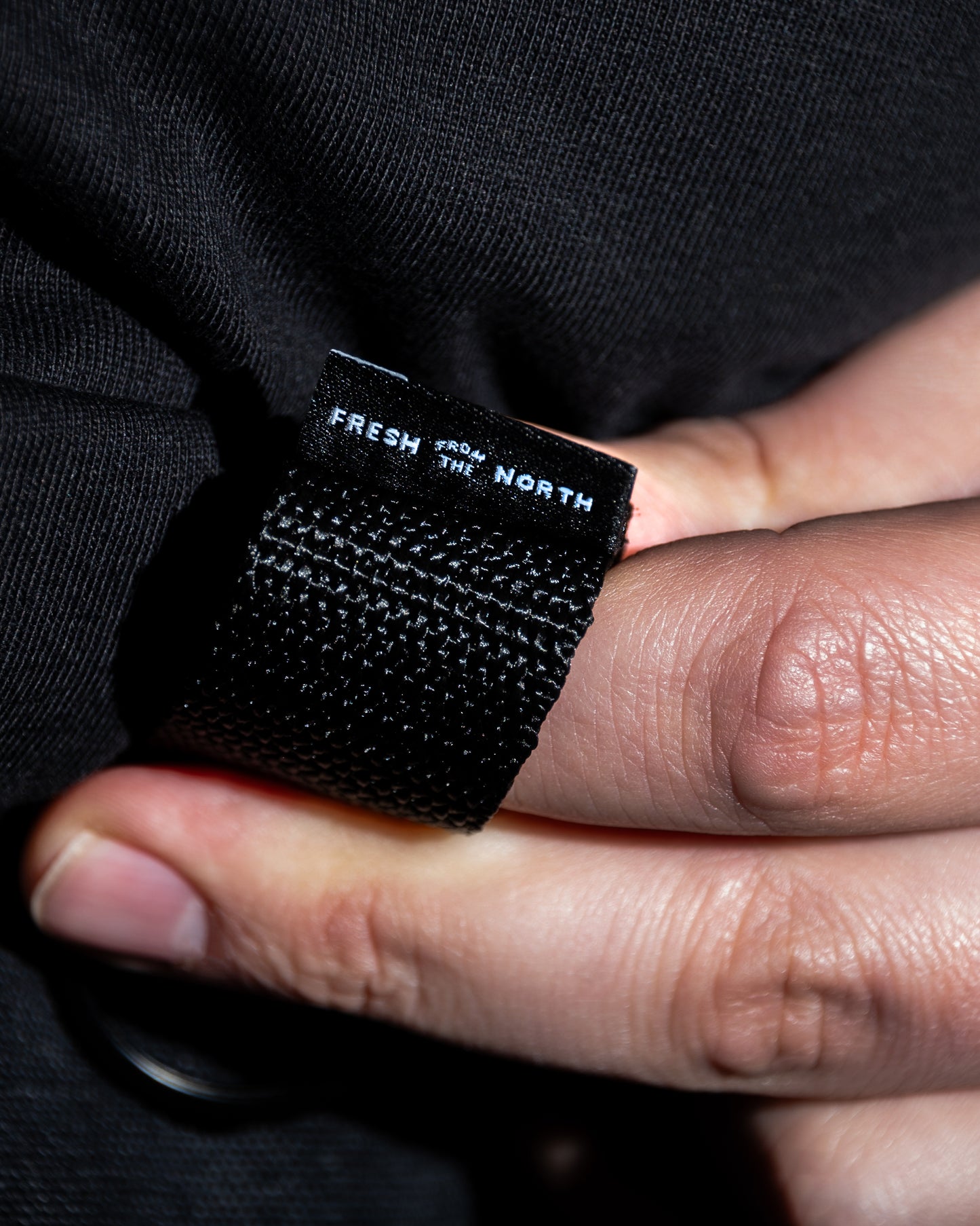 Close-up of a black woven label with 'Fresh from the North' text on a dark fabric background.