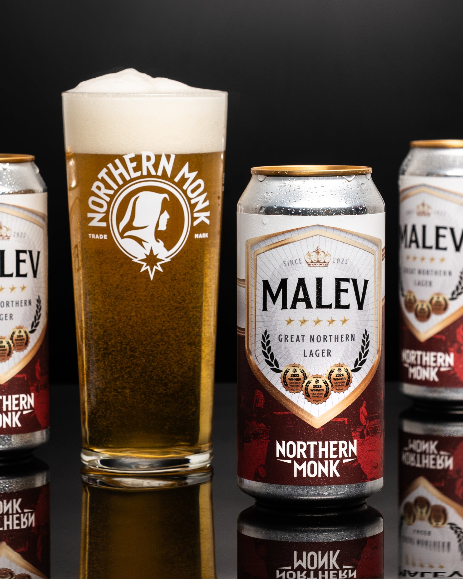 Northern Monk Malev lager cans and a glass of beer on a black background