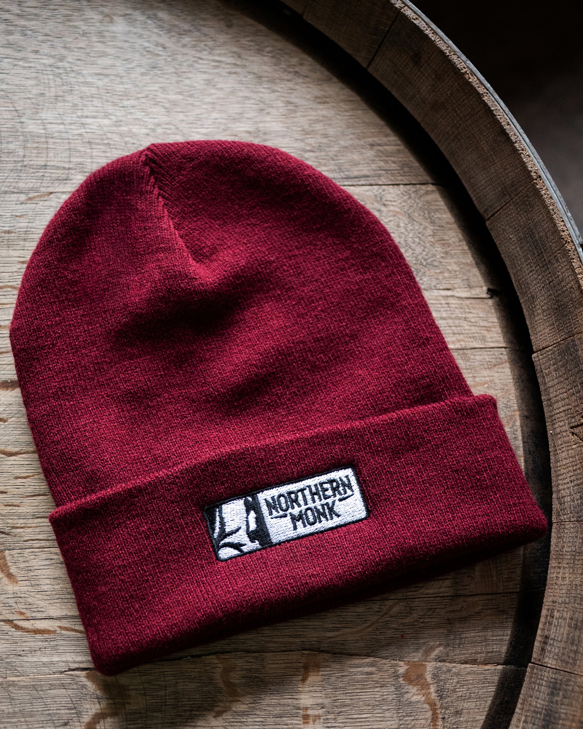 Burgundy beanie with a Northern Monk embroidered on a wooden surface