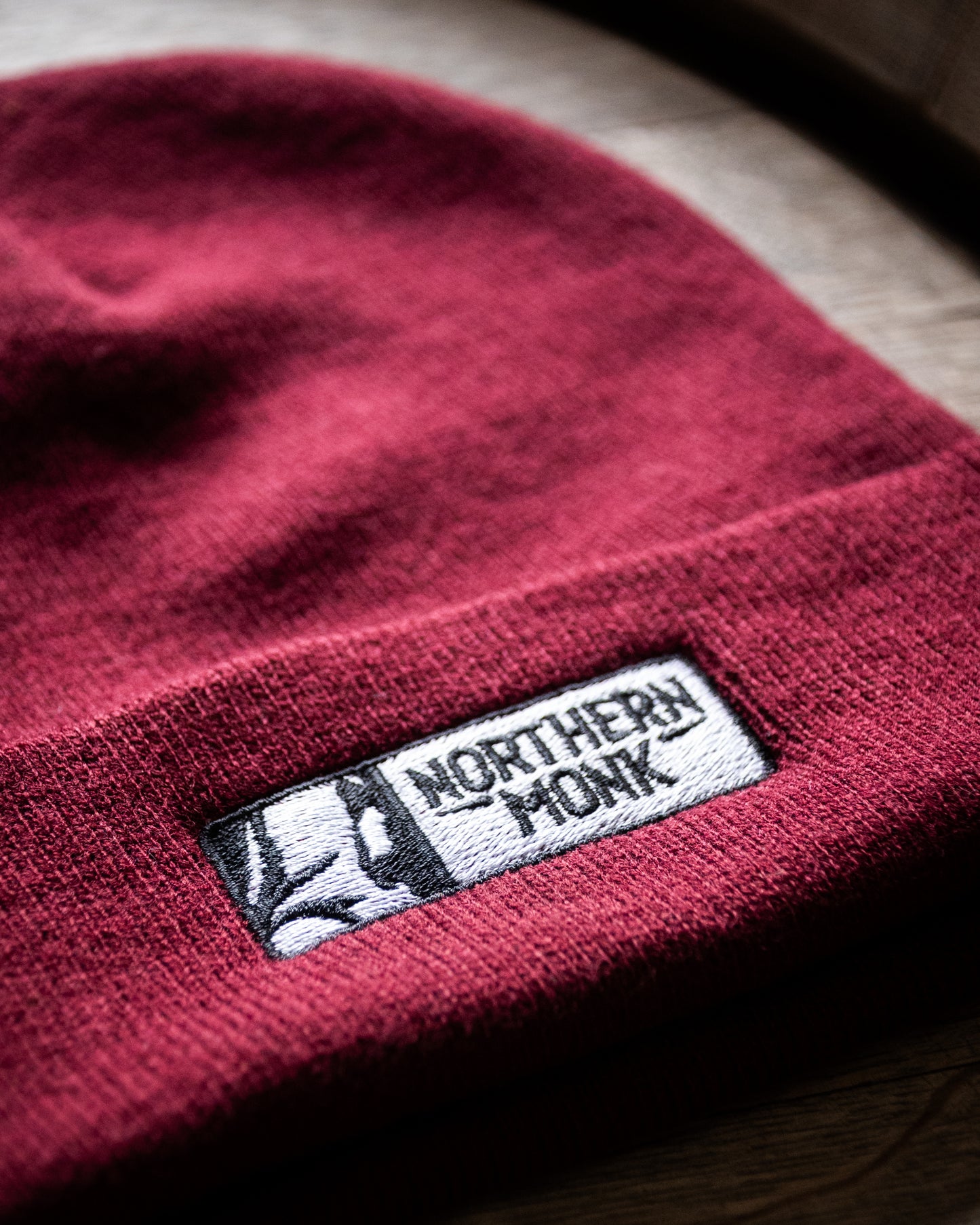 Burgundy beanie with a 'Northern Monk' label on a wooden surface
