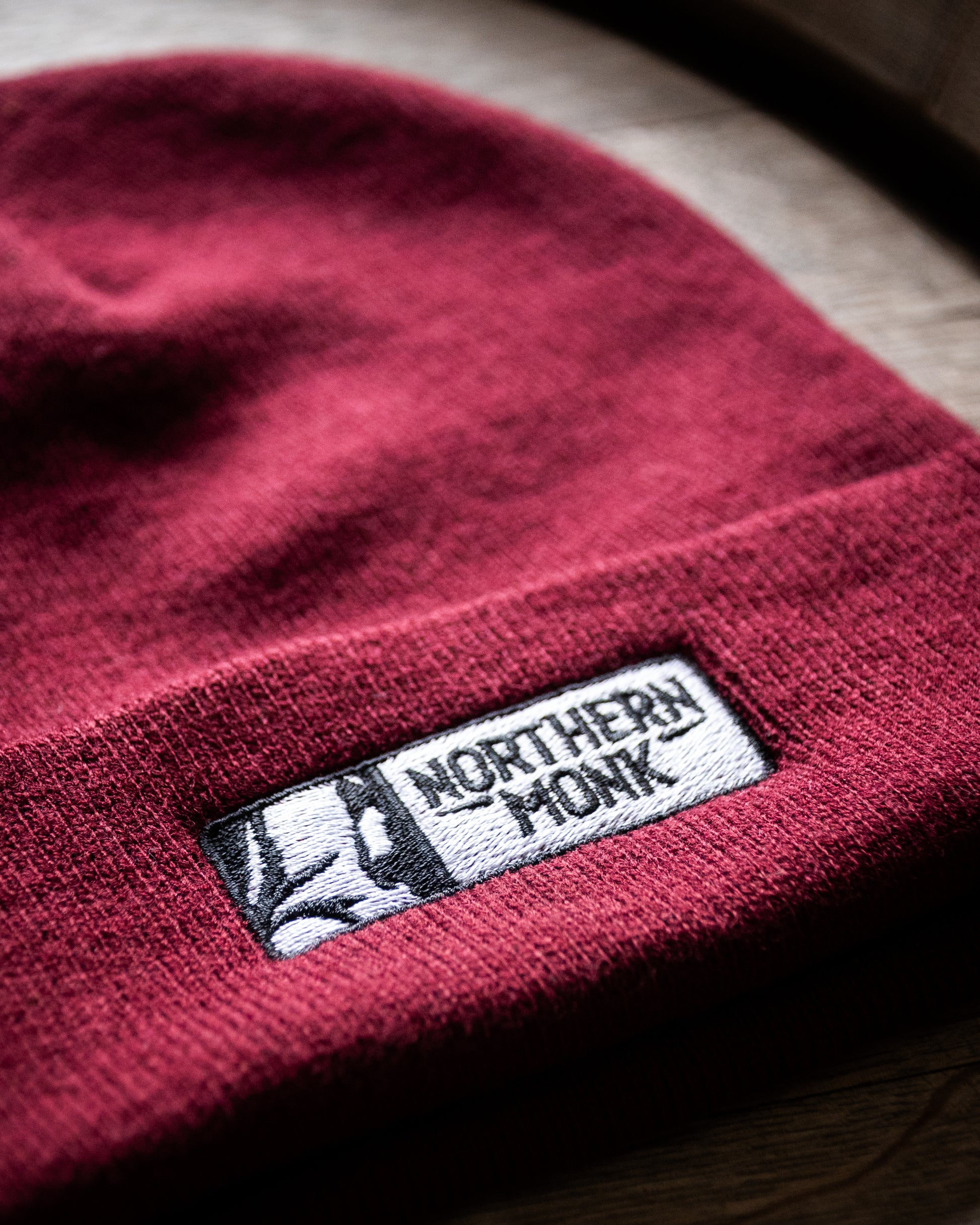 Burgundy beanie with a 'Northern Monk' label on a wooden surface