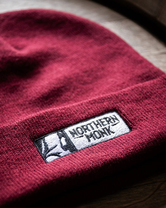 Burgundy beanie with a 'Northern Monk' label on a wooden surface