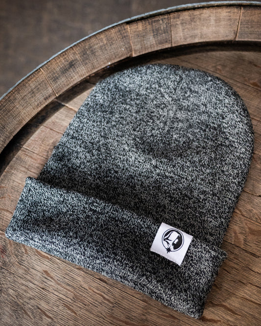 Grey beanie with a Northern Monk logo tab on a wooden surface