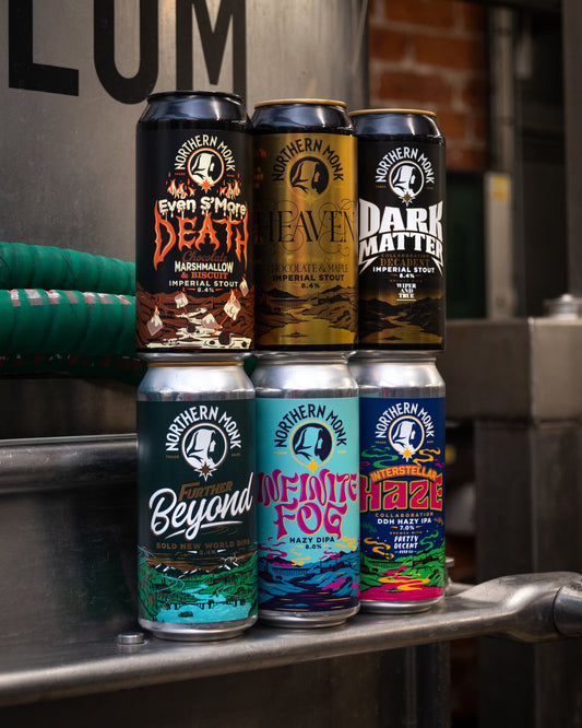 Collection of Northern Monk beer cans stacked on a metal surface with a blurred background.