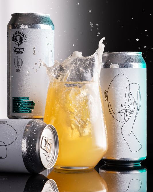 Cans of Reimagined with a glass of beer in the center on a dark background